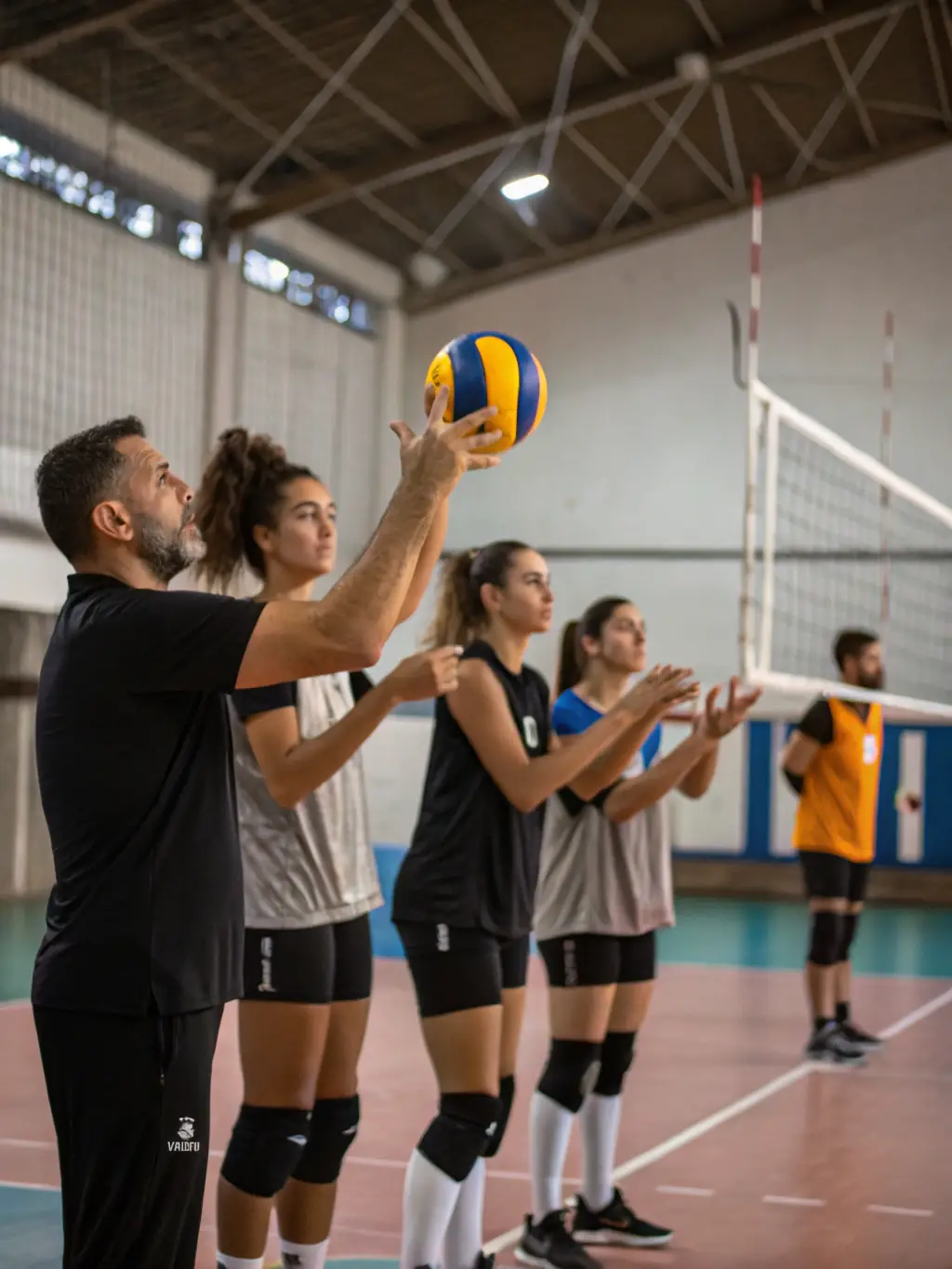 Image of coaches leading a volleyball clinic, demonstrating techniques and providing personalized feedback, with participants actively engaged in the training.